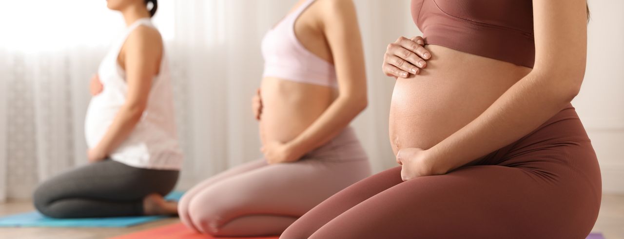 Drei schwangere Frauen knien auf Yogamatten. Sie halten ihren Bauch und haben die Augen geschlossen.