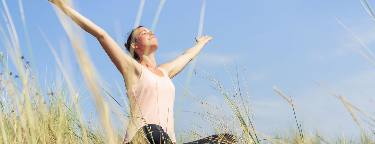 Une femme est assise en tailleur, les bras tendus, l'expression du visage détendue et un léger sourire sur les lèvres.