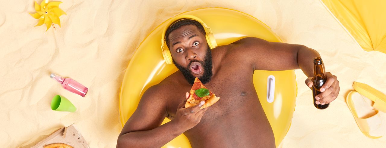 Mann im Schwimmring mit Pizza und Bier am Strand