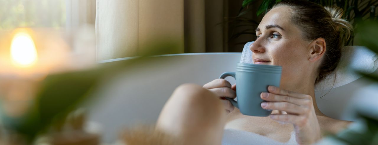 Frau in einer Badewanne mit Tasse in der Hand