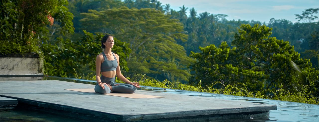 Frau sitzt im Schneidersitz in der Natur und macht Yoga