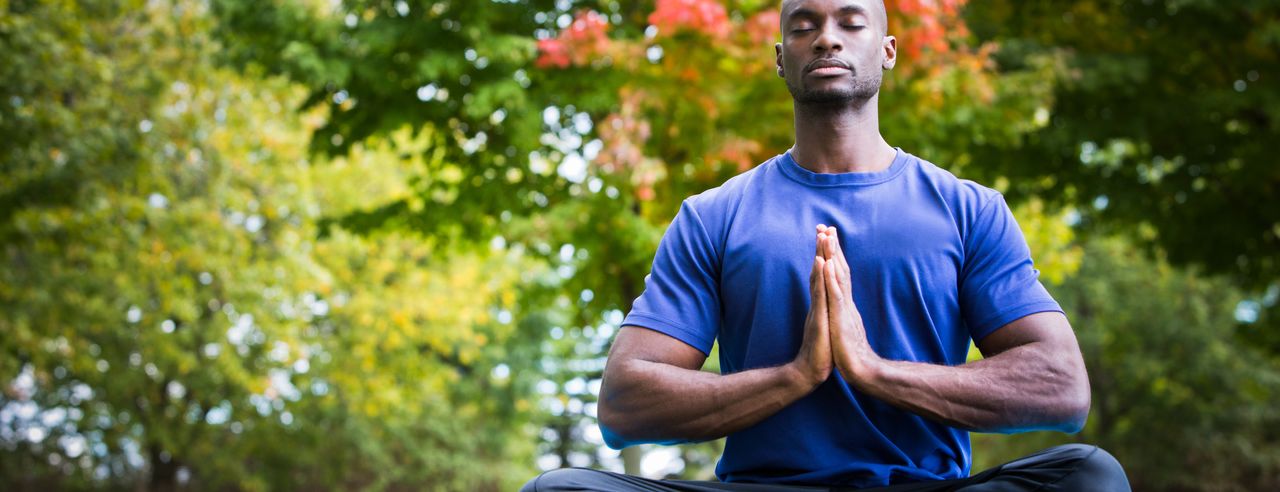 Mann meditiert auf Yogamatte im Park