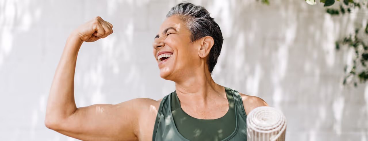 Eine Frau mit Yogamatte unterm Arm zeigt ihre Muskeln