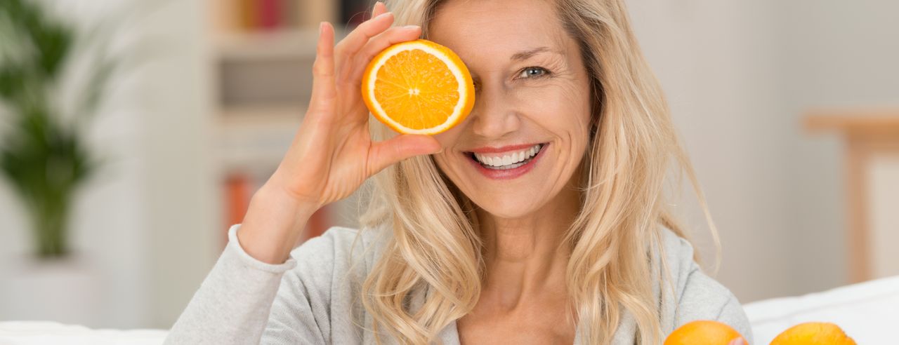 Lachende Frau hält Orangen in die Kamera