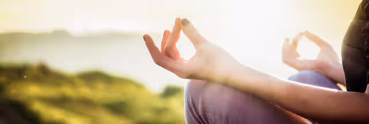 Yoga und Achtsamkeit; Eine  Frau sitzt im Lotussitz bei Sonnenschein