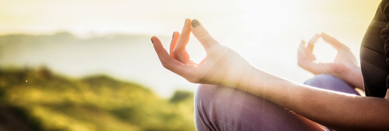 Yoga und Achtsamkeit; Eine  Frau sitzt im Lotussitz bei Sonnenschein