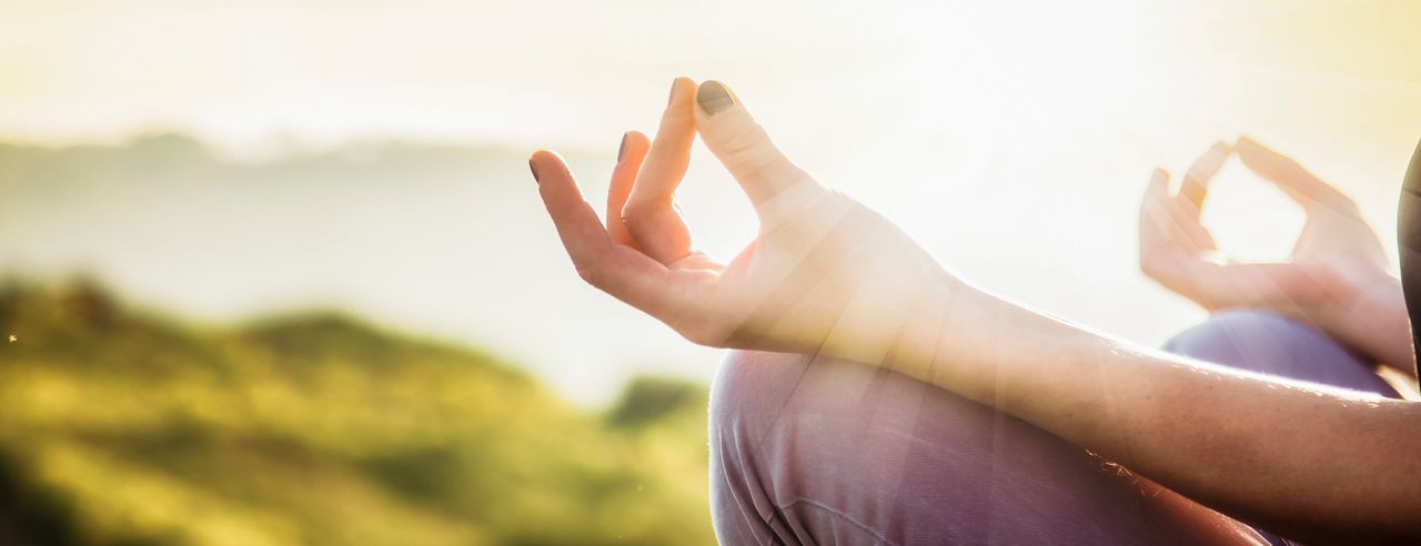 Yoga und Achtsamkeit; Eine  Frau sitzt im Lotussitz bei Sonnenschein