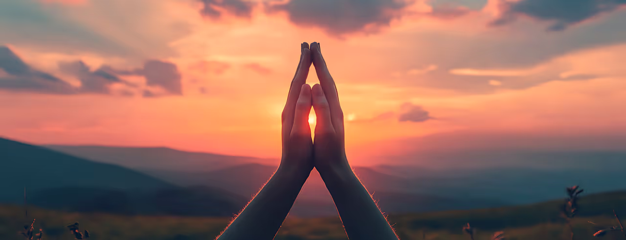 Silueta de manos cruzadas en oración al atardecer