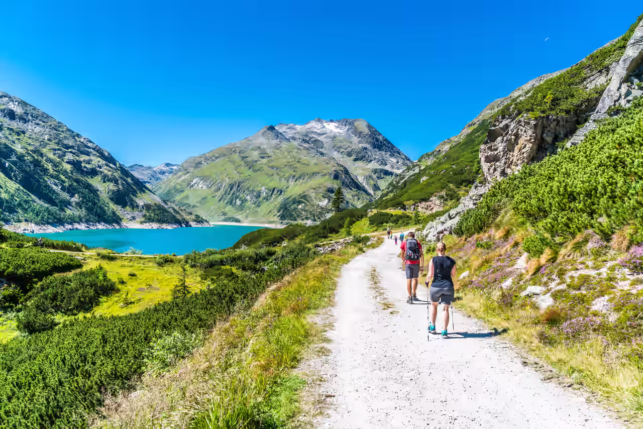 Verschiedene Wanderer, die in sommerlicher Wanderkleidung und mit Stöcken am See wandern
