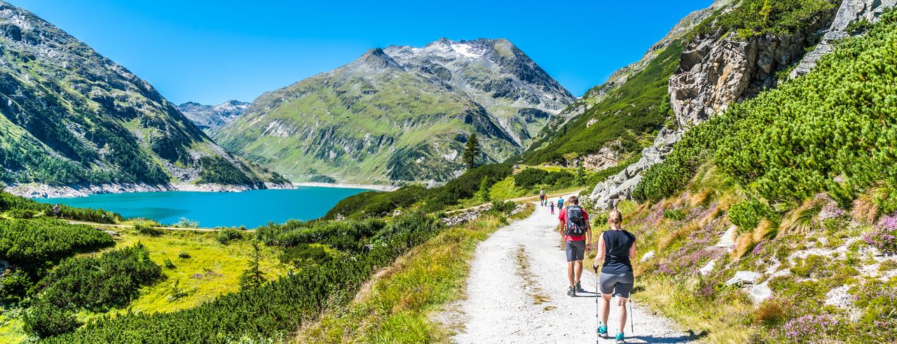 Verschiedene Wanderer, die in sommerlicher Wanderkleidung und mit Stöcken am See wandern