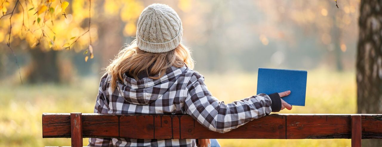 Eine Frau sitzt auf einer Parkbank mit Buch in der Hand