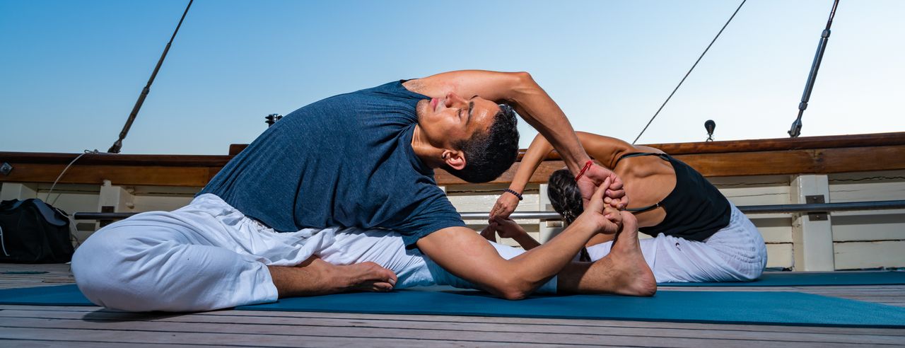Ein Mann und eine Frau machen Yoga auf einem Segelboot