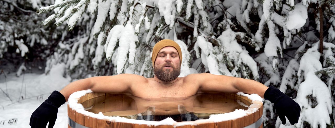 Ein Mann in einer Eistonne vor einer verschneiten Tanne.