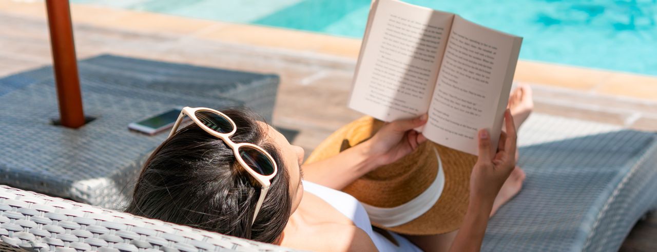 Alleinreisende Frau sitzt am Pool und liest ein Buch