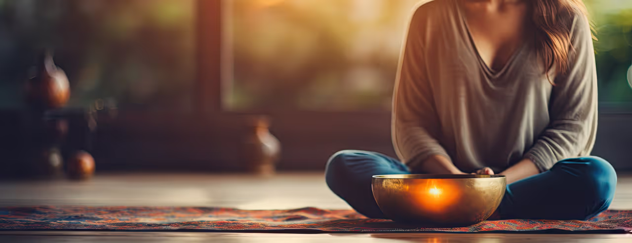 A woman sits cross-legged in front of a golden bowl 