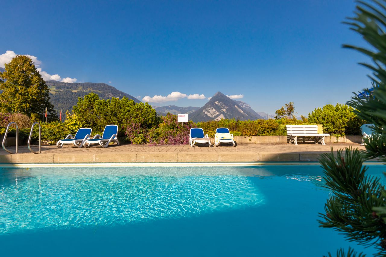 Pool mit Sonnenliegen vor Bergen
