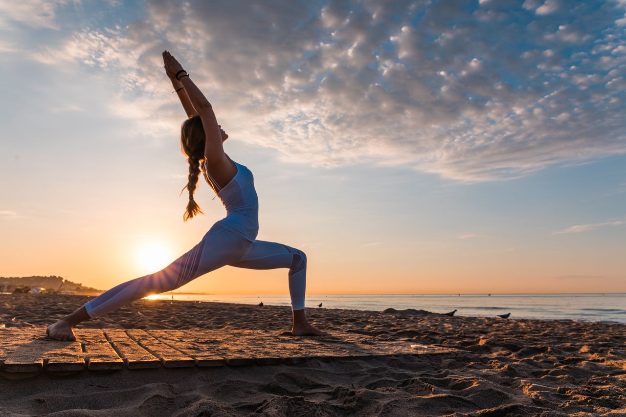 Frau macht am Strand bei Sonnenuntergang Yoga