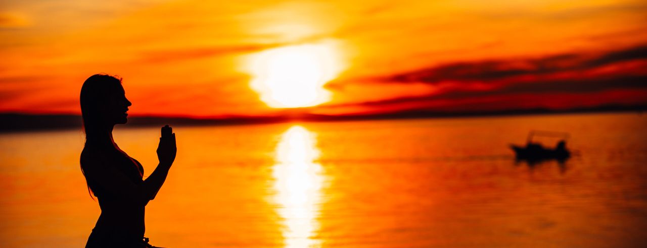 Silhouette einer Frau in meditativer Haltung mit Sonnenuntergang im Hintergrund