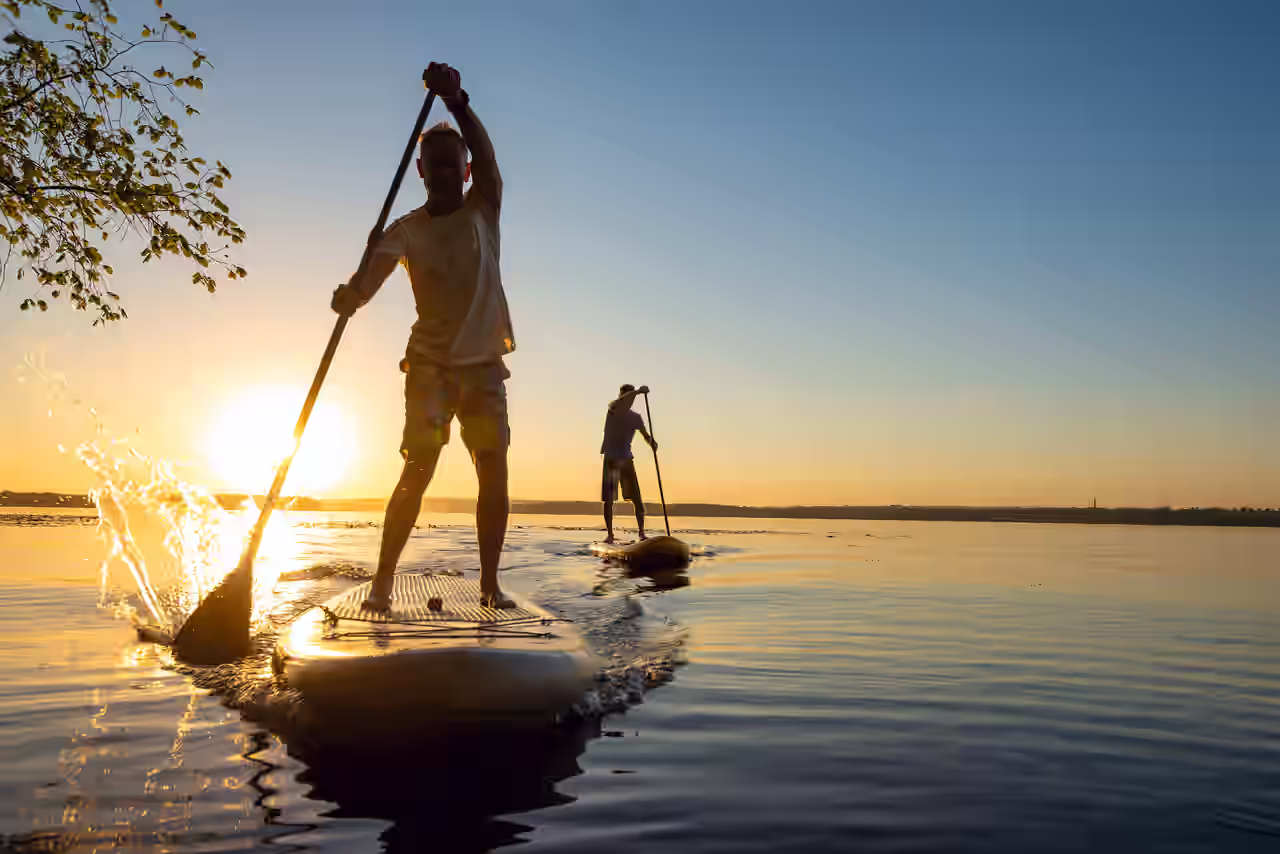 Zwei Personen mit SUP-Board bei Sonnenuntergang