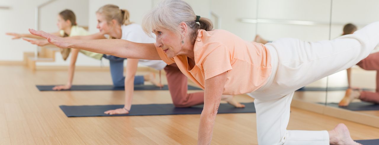 Ältere Damen machen in einem Kurs gemeinsam Yoga Übungen.