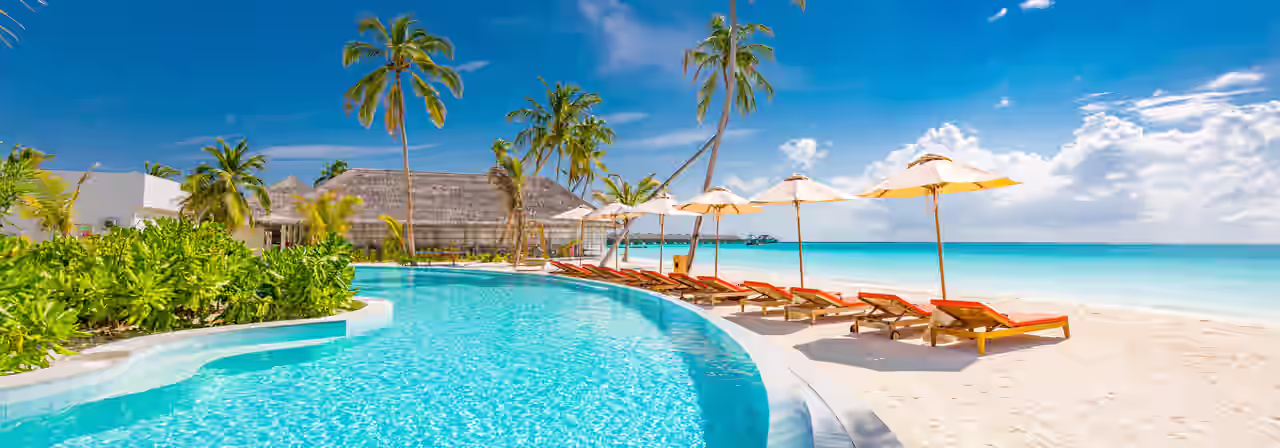 Pool am Meer mit Palmen, Sonnenschirmen und Liegen