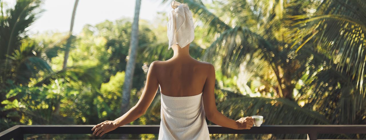 Eine Frau steht auf der Dachterrasse eines Wellness Resorts und genießt den Blick auf Palmen