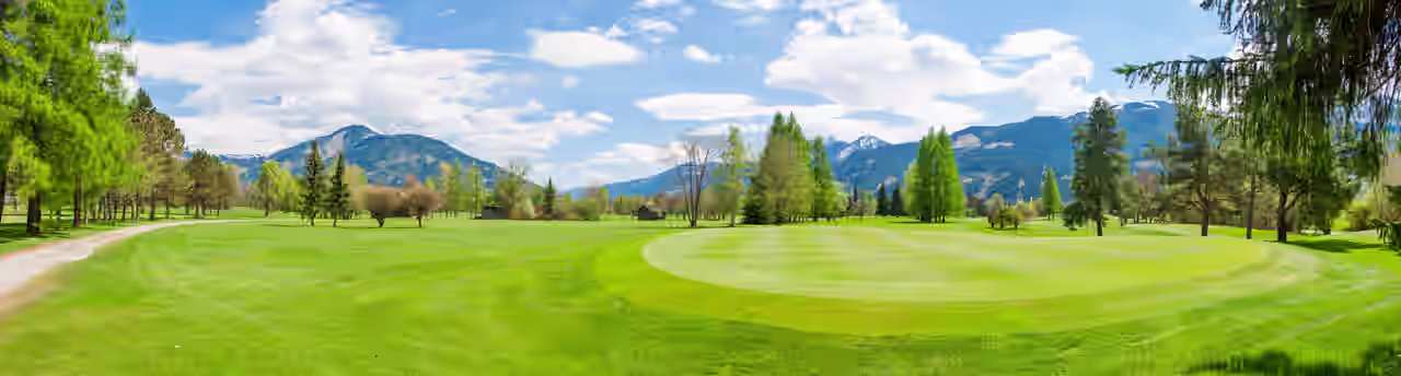 Golfplatz mit Bäumen und Bergen im Hintergrund