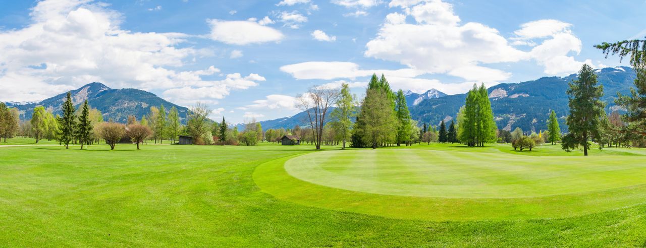 Golfplatz mit Bäumen und Bergen im Hintergrund