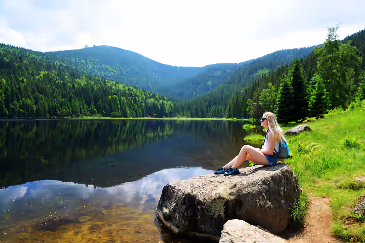 Touristin sitzt auf einem großen Stein am See im Bayerischen Wald
