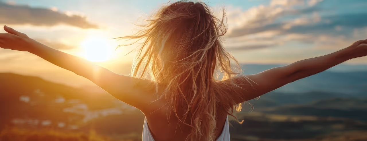 Frau hält die Arme ausgestreckt im Sonnenuntergang