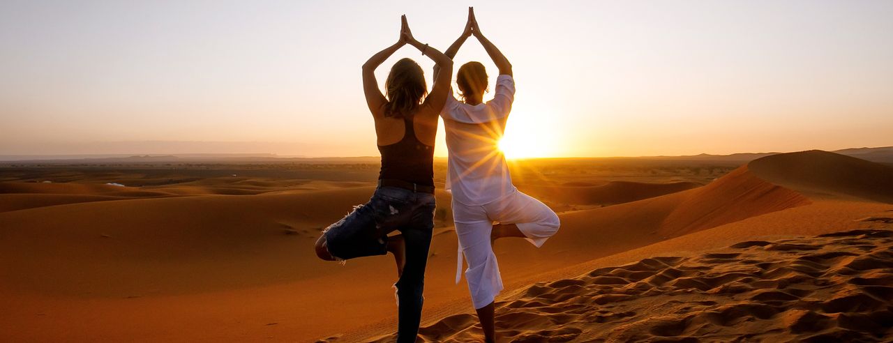 Zwei Frauen in der Wüste in der Baum Yoga-Pose
