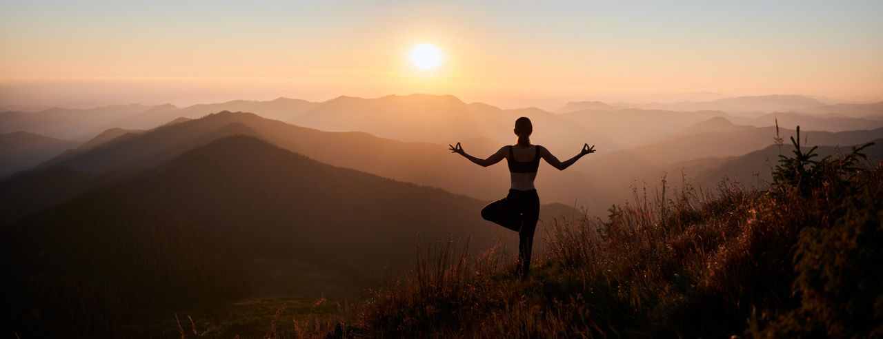 Eine Frau ist durch Akupunktur ausgeglichen und steht in Yoga Pose vor einem Sonnenaufgang