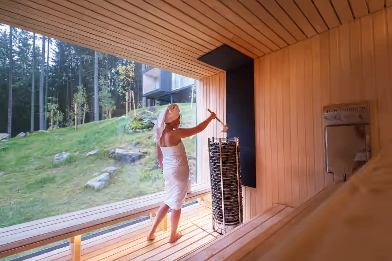 Eine Frau macht einen Aufguss in einer Sauna mit Waldblick