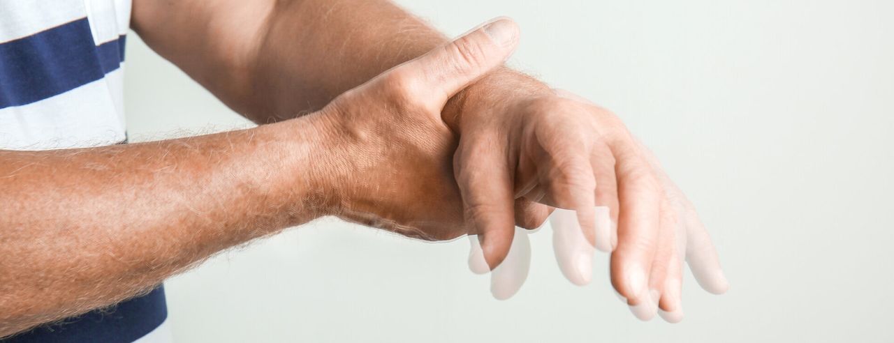 Alter Mann mit Parkinson hält sich die Hand