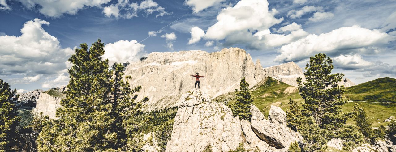 Eine Frau praktiziert Yoga in den Bergen Tirols. Die Sonne scheint und es sind Wolken am Himmel zu sehen.