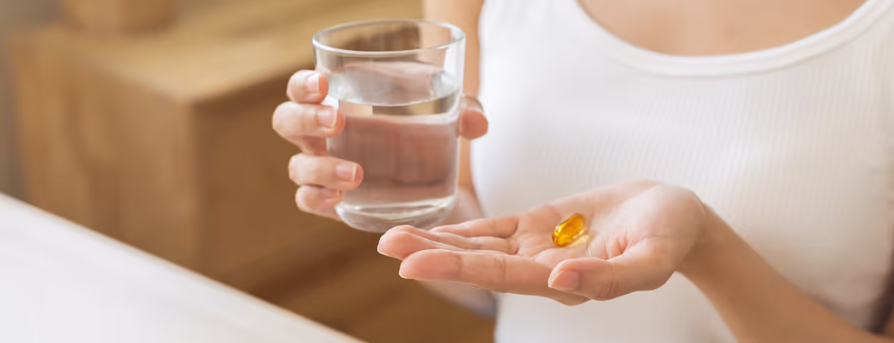 Frau hält in der linken Hand eine Kapsel und in der rechten ein Wasserglas