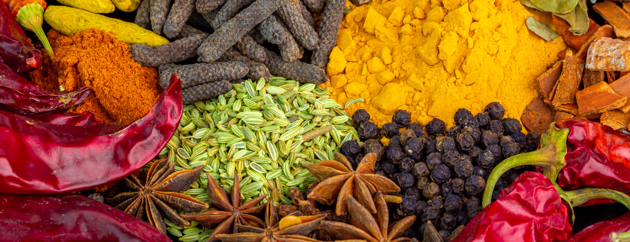Red, yellow, green and brown dried spices are placed together in a bowl.