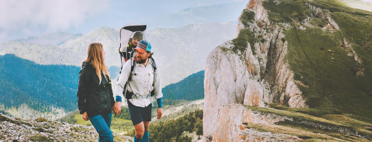 Ein Paar beim Wandern in den Bergen, mit Kind in der Wandertrage