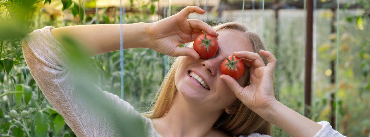 Eine fröhliche Frau hält sich Tomaten vor die Augen