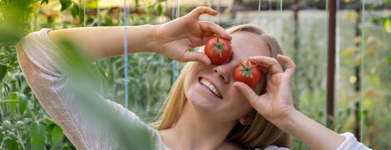 Eine fröhliche Frau hält sich Tomaten vor die Augen