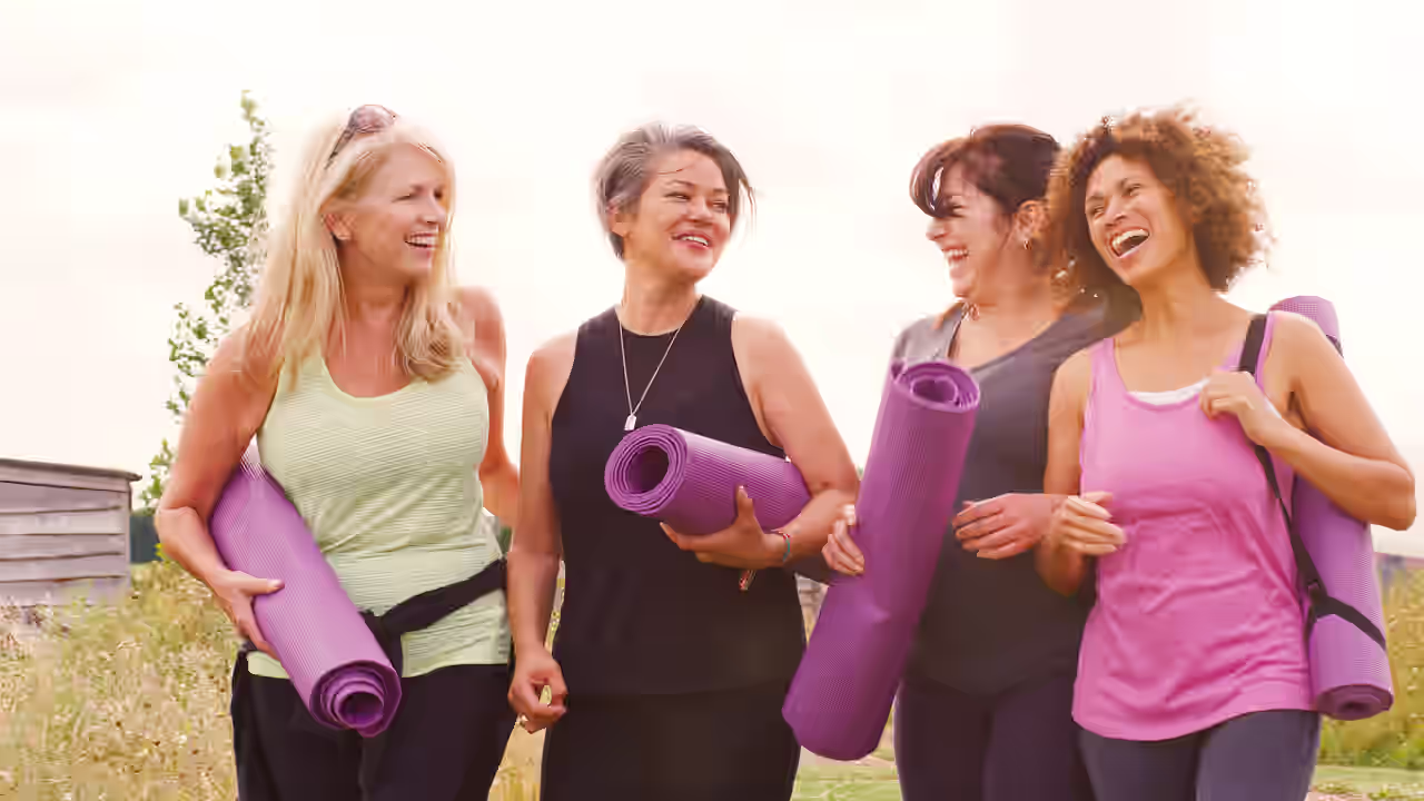 Gruppe von lachenden Frauen mittleren Alters mit lilafarbenen Yogamatten