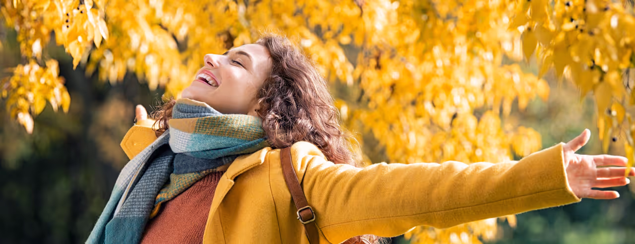 Eine glückliche Frau hebt beim Herbstspaziergang die Arme in die Luft