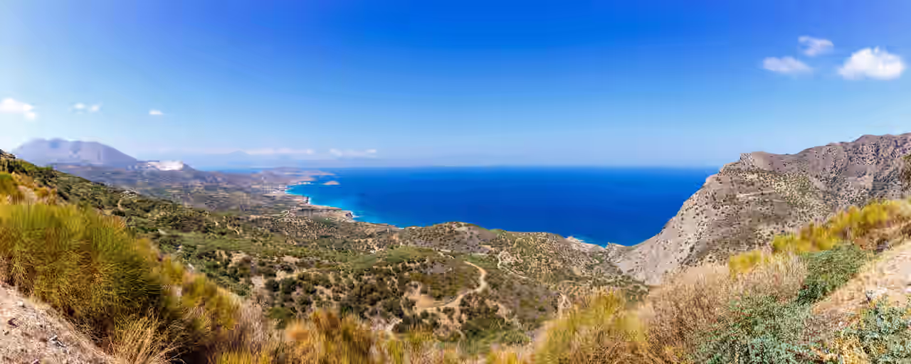 Panorama der Landschaft auf Kreta mit Blick über bewachsene sandige Hügel auf das tiefblaue Meer