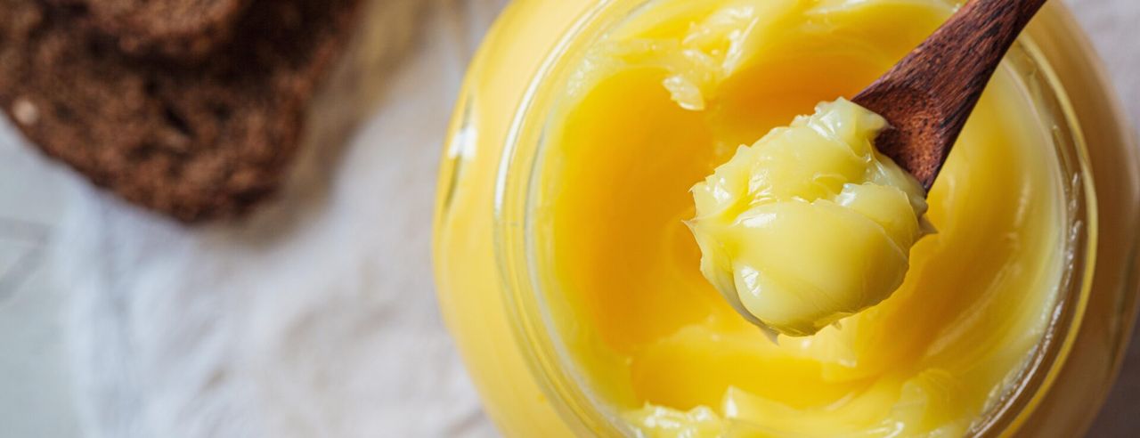 Ghee wird mit einem Holzlöffel aus einem Glas entnommen