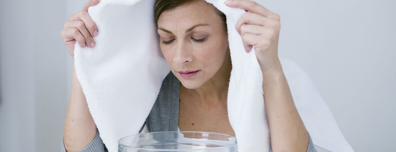 Femme avec une serviette sur la tête, penchée sur une clé en verre pour inhalation