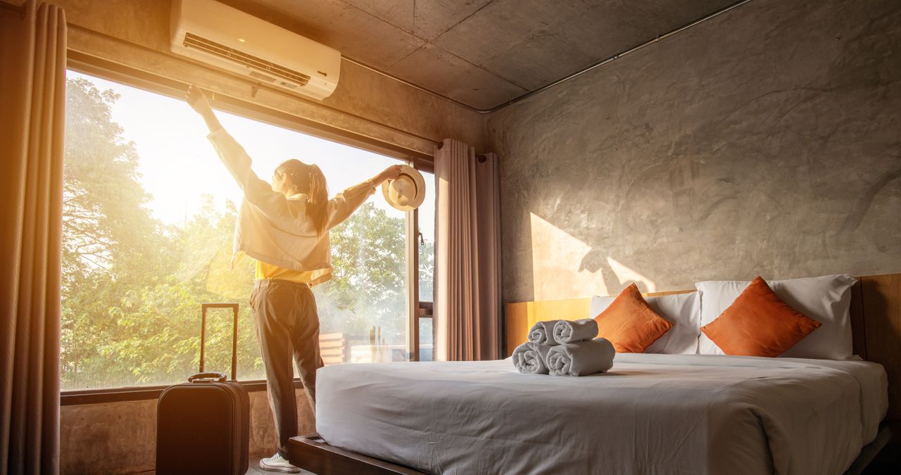 Eine Frau steht mit erhobenen Armen am Fenster eines klimatisierten Hotelzimmers