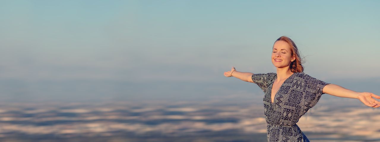 Eine fröhliche Frau Breitet die Arme aus vor einem Natur-Panorama