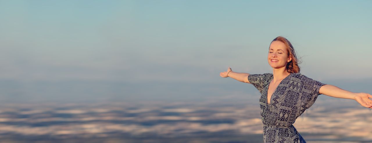 Eine fröhliche Frau Breitet die Arme aus vor einem Natur-Panorama