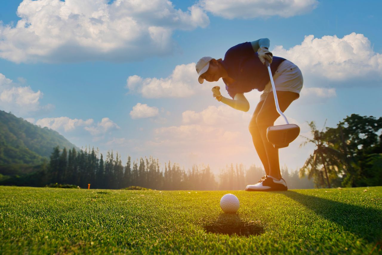 Eine Frau freut sich auf dem Golfplatz, dass ihr Ball ins Loch geht