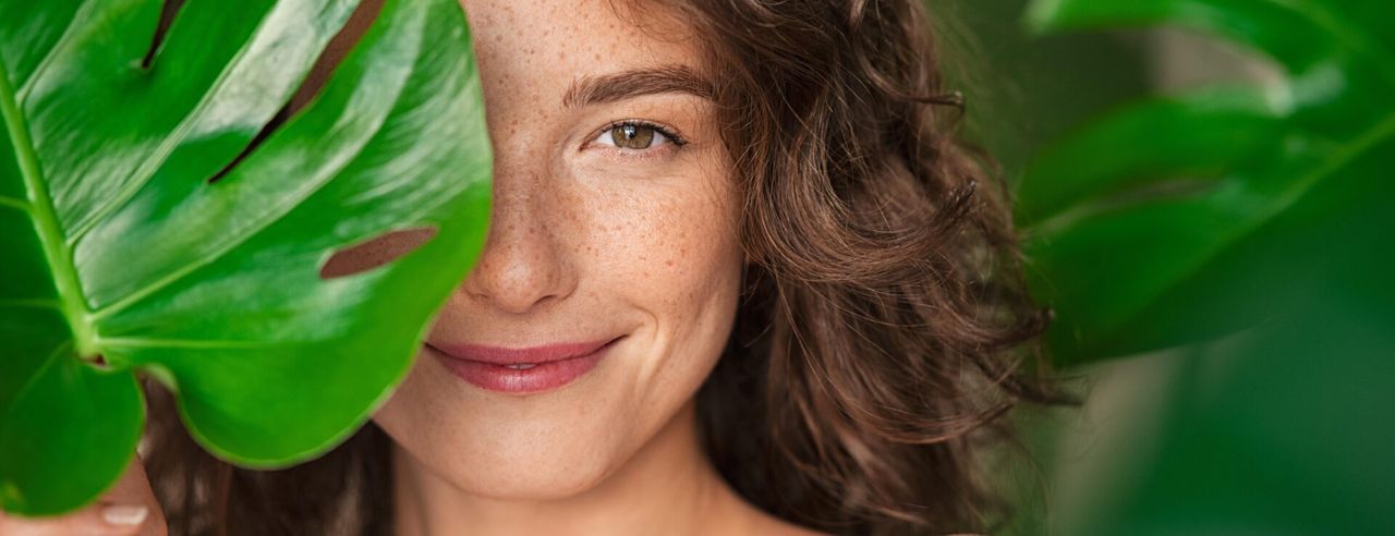 Frau, die hinter Blatt in die Kamera schaut